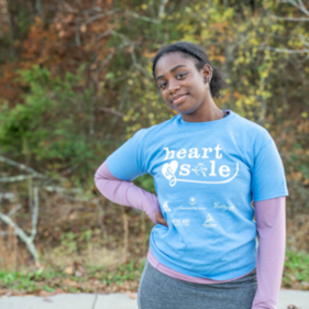 A Girls on the Run participant smiles at the camera in a blue Heart & Sole practice shirt.